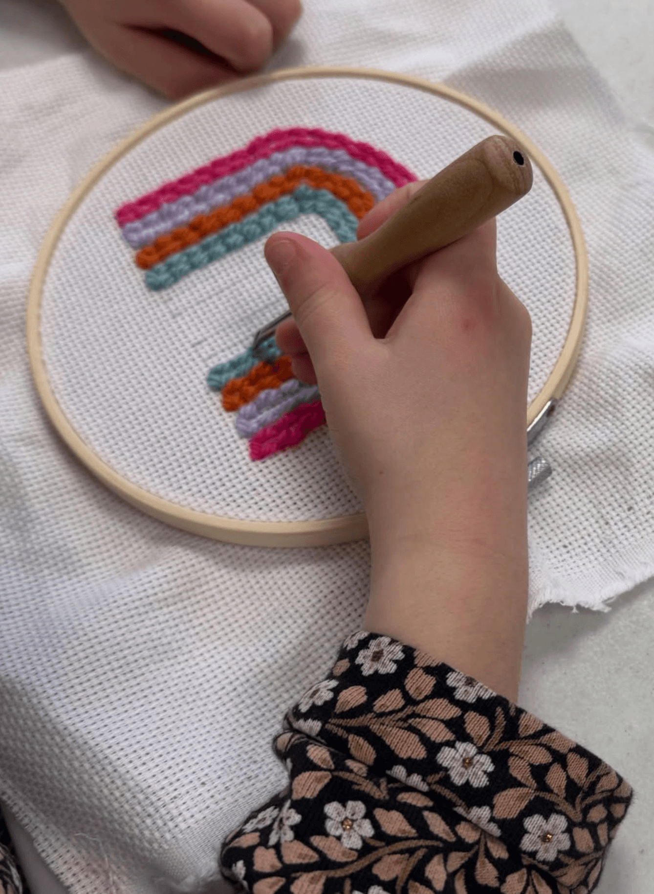 Enfant réalisant un arc-en-ciel en punch needle lors d'un atelier créatif à Fontaine-le-Comte